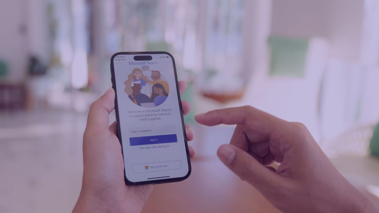 A person holding a smartphone displaying a family social app interface, with options to sign up. Soft focus background suggests a cozy indoor setting.