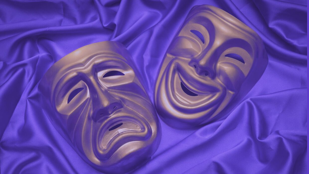 Two theatrical masks placed on a purple satin fabric: one mask represents comedy with a smiling expression, while the other represents tragedy with a frowning expression.