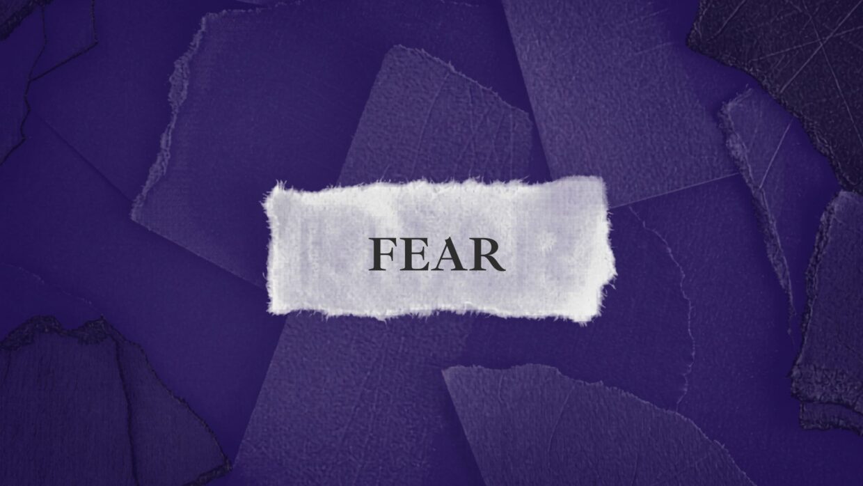 A textured background featuring various shades of purple with torn paper edges. In the center, a white strip of paper displays the word "FEAR" in bold, black letters.