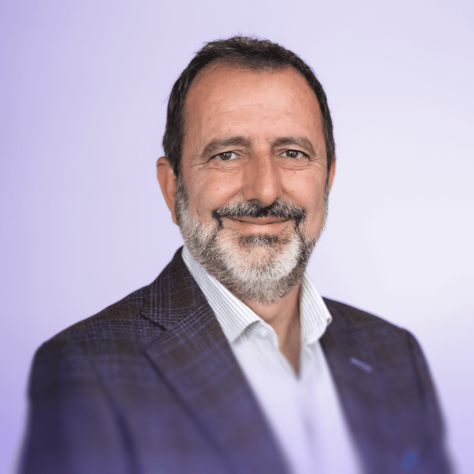 Roberto Veiga, smiling while wearing a light blue dress shirt, standing in front of a white wall.