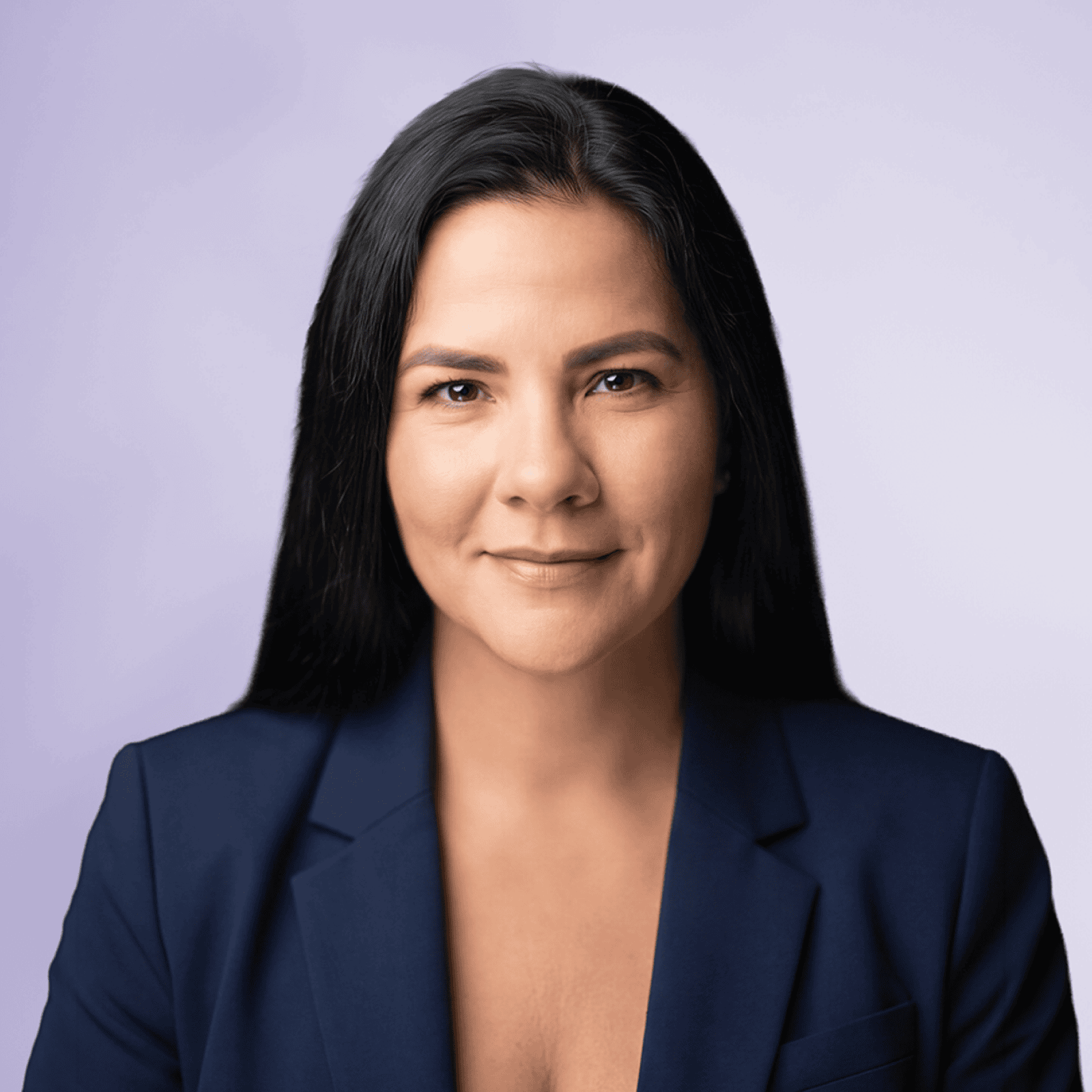 A woman with long dark hair wears a navy blazer against a light purple background.